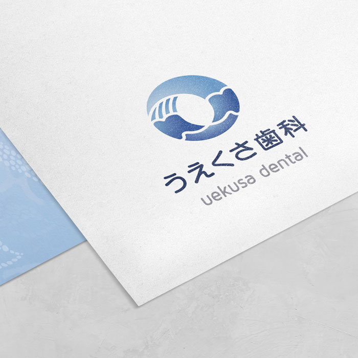 テクスチャのある用紙に施された『うえくさ歯科』のロゴデザイン。青い円形の波のシンボルが特徴的な、TMCreationによる歯科ブランディングの制作事例。